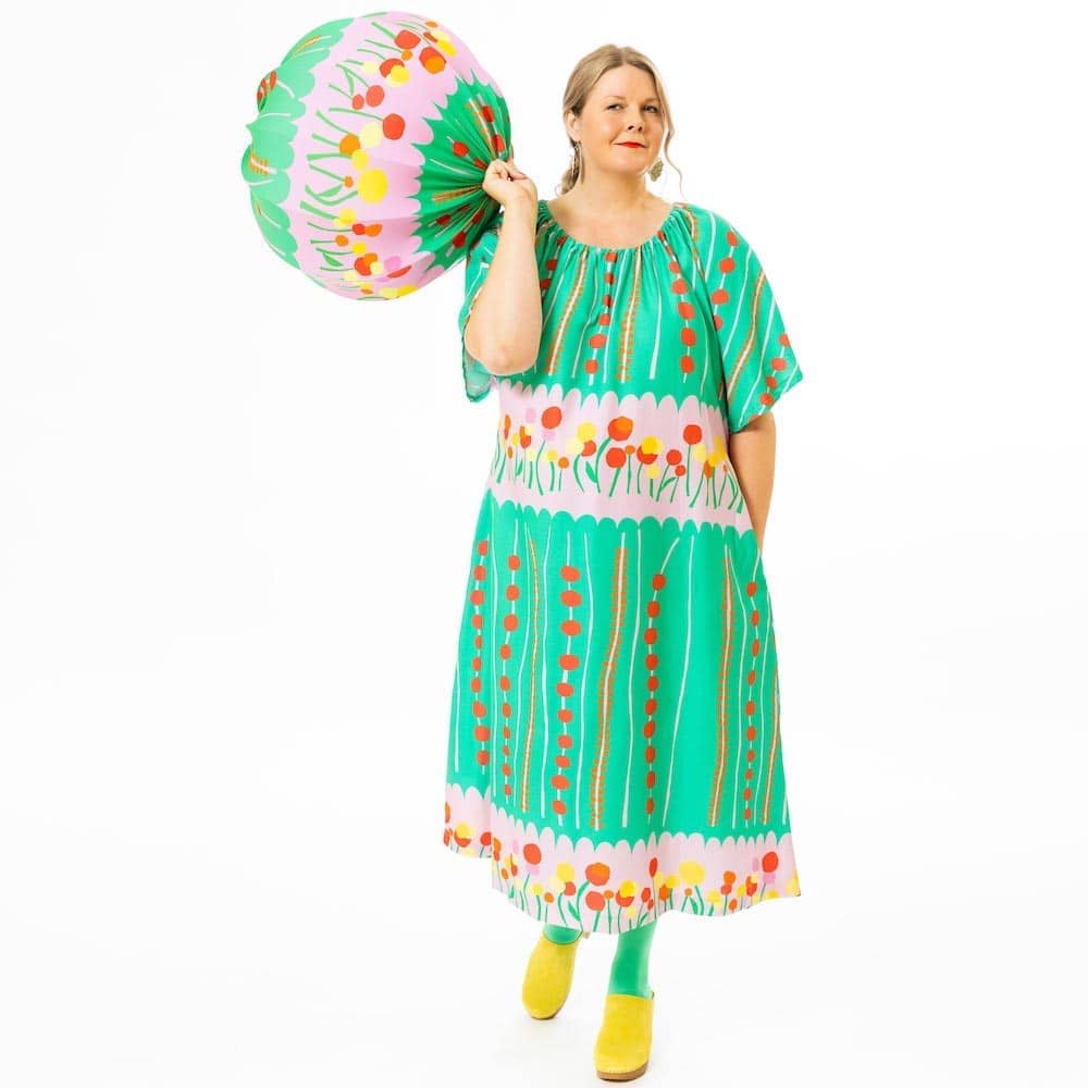 Kotimainen Virkkukoukkusen Satiininen juhlava Loippana-mekko heleällä vihreä-pinkillä Kesäheinäkuosilla. Kuosissa pystyraitaisessa Kesäheinässä punaisia marjoja ja vaakasuuntaisissa vaaleanpunaisissa palkeissa kauniita pallomaisia kukkia punaisina, oransseina ja keltaisina.